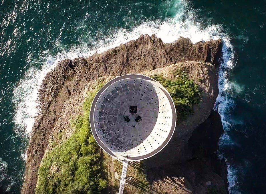 Aerial view of the circular La Copa del Sol structure on its promontory above the ocean