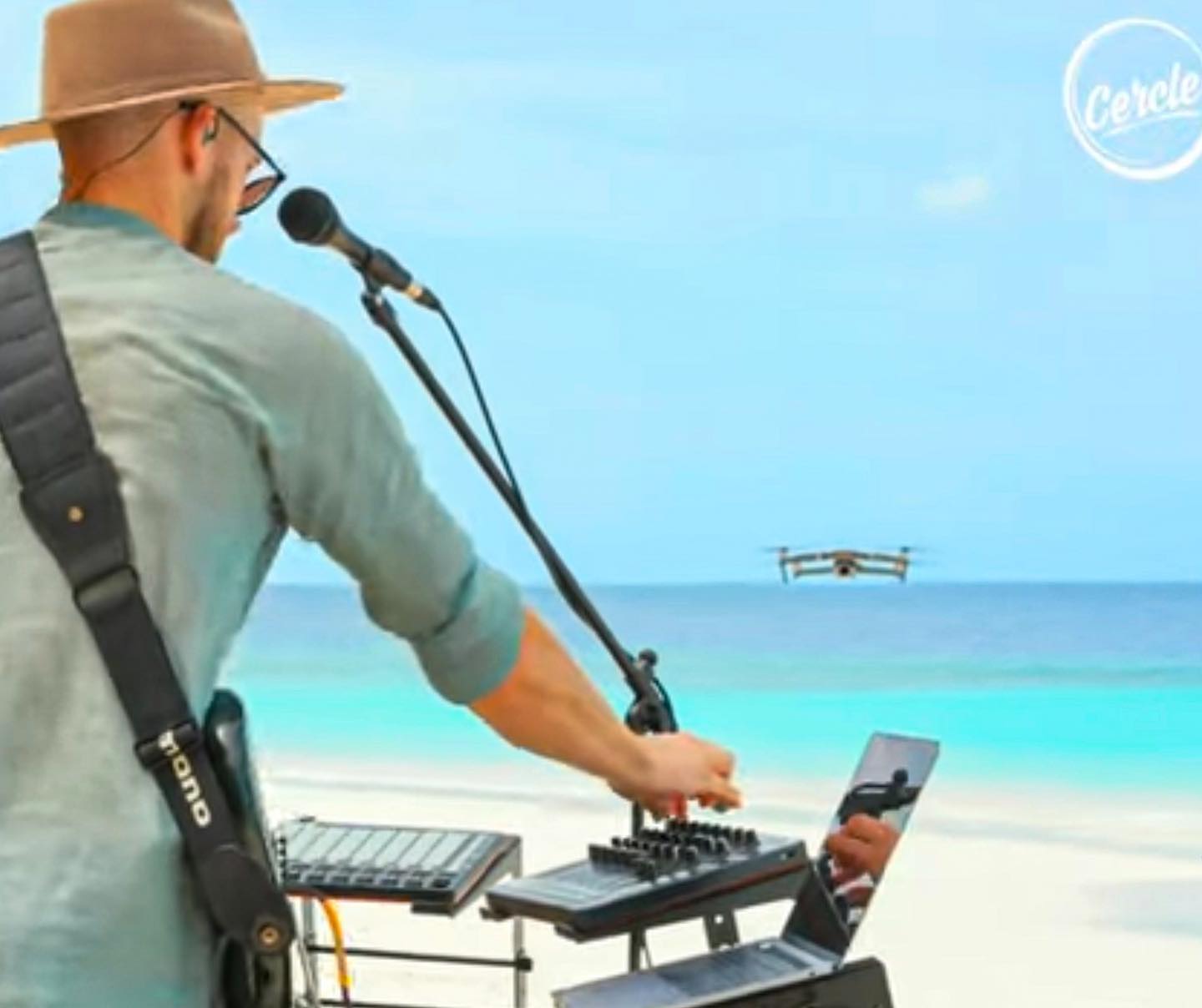 Monolink at the microphone in front of his instruments, with a turquoise Maldivian lagoon behind him