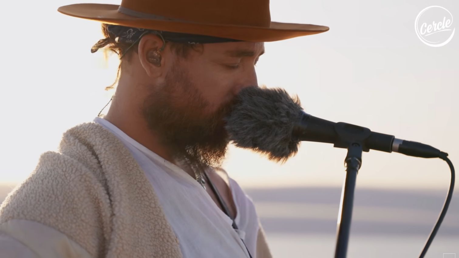 RY X singing into a microphone and wearing a hat during his Cercle session at Lençóis Maranhenses